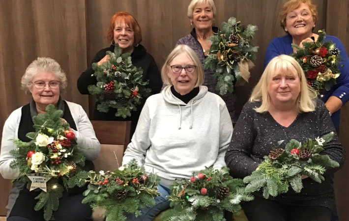 six women sitting down holding Christmas wreaths