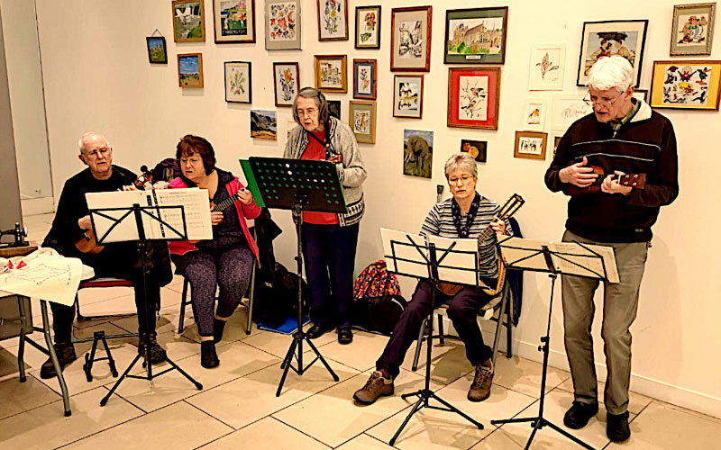 Five people playing ukulele inside 
