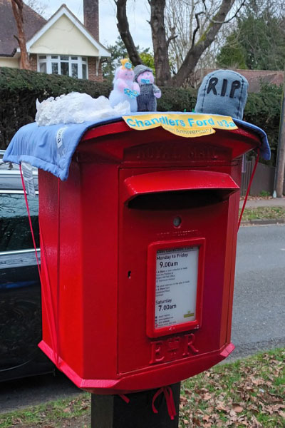 A small postbox with a cover on the top which shows fabric models getting married and a tombstone saying RIP