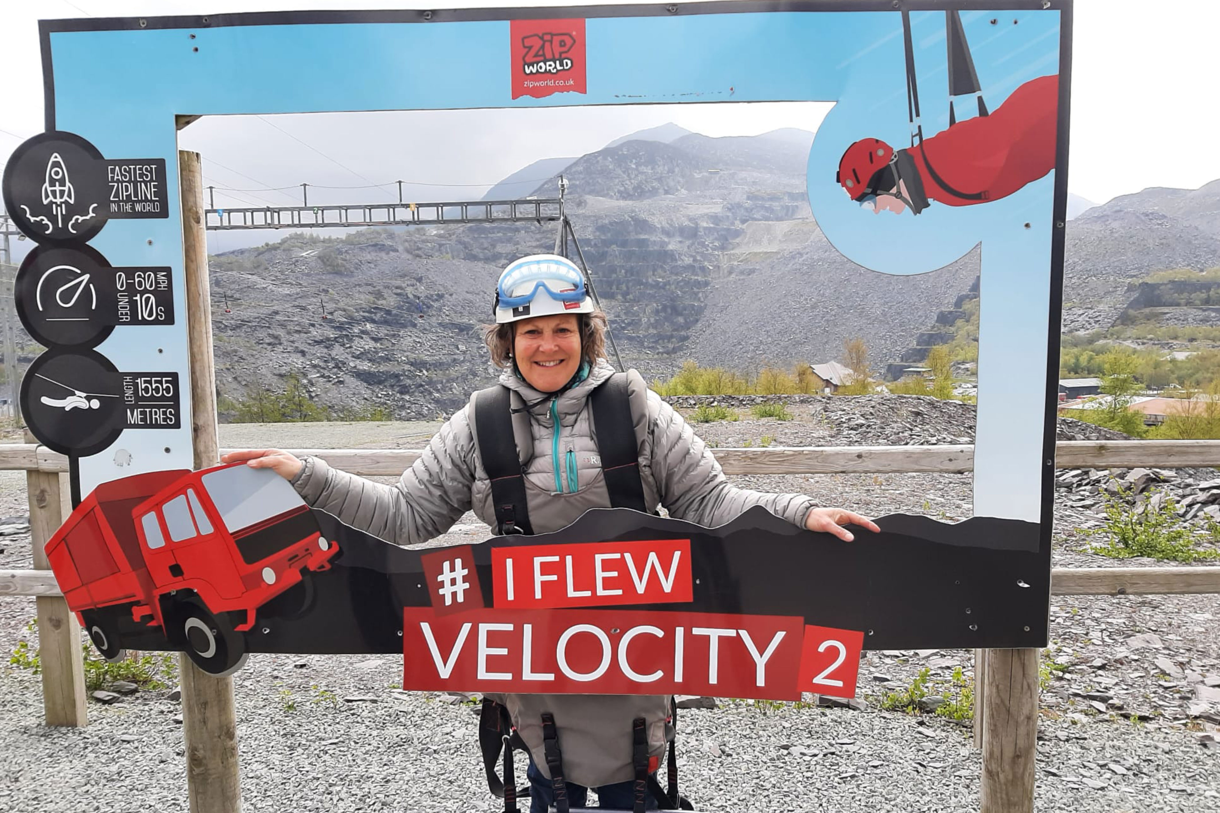 A woman standing in front of a dramatic view. She is wearing a helmet and is standing in front of a picture frame that says 'I flew velocity.'