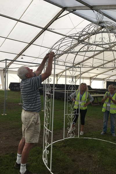 A man installing a giant bird cage in a marquee