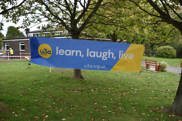 A u3a learn laugh live banner suspended by trees