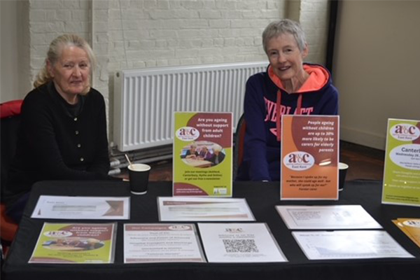 Two women, including Penny on the right, sitting behind a table that has posters and leaflets about awoc.