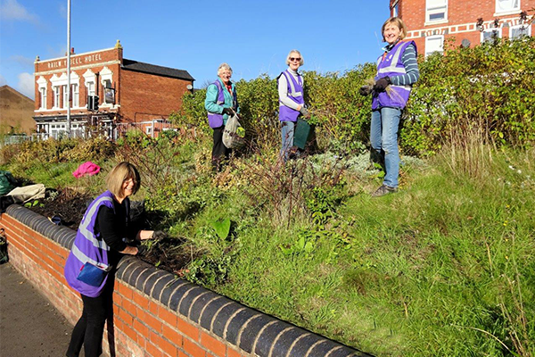 Four u3a members wearing purple high vis jackets gardening in a bank at Kidderminster station