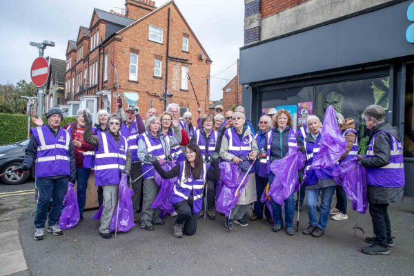 A large group of people standing on a high street wearing bright purple lanyards. They all look very jolly and are posing for the camera.