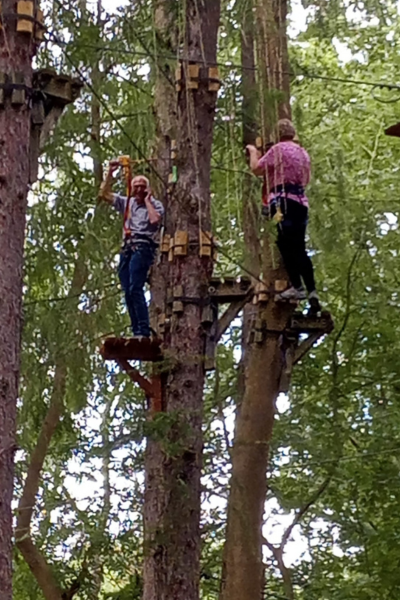 Two u3a members are at an outdoor adventure park, high up in the trees