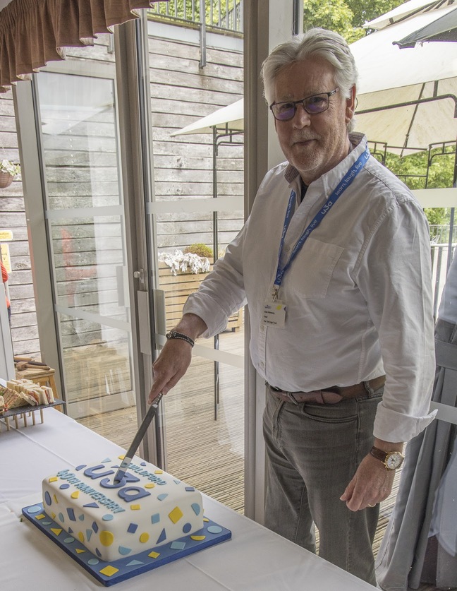 man looking at camera cutting into u3a branded cake