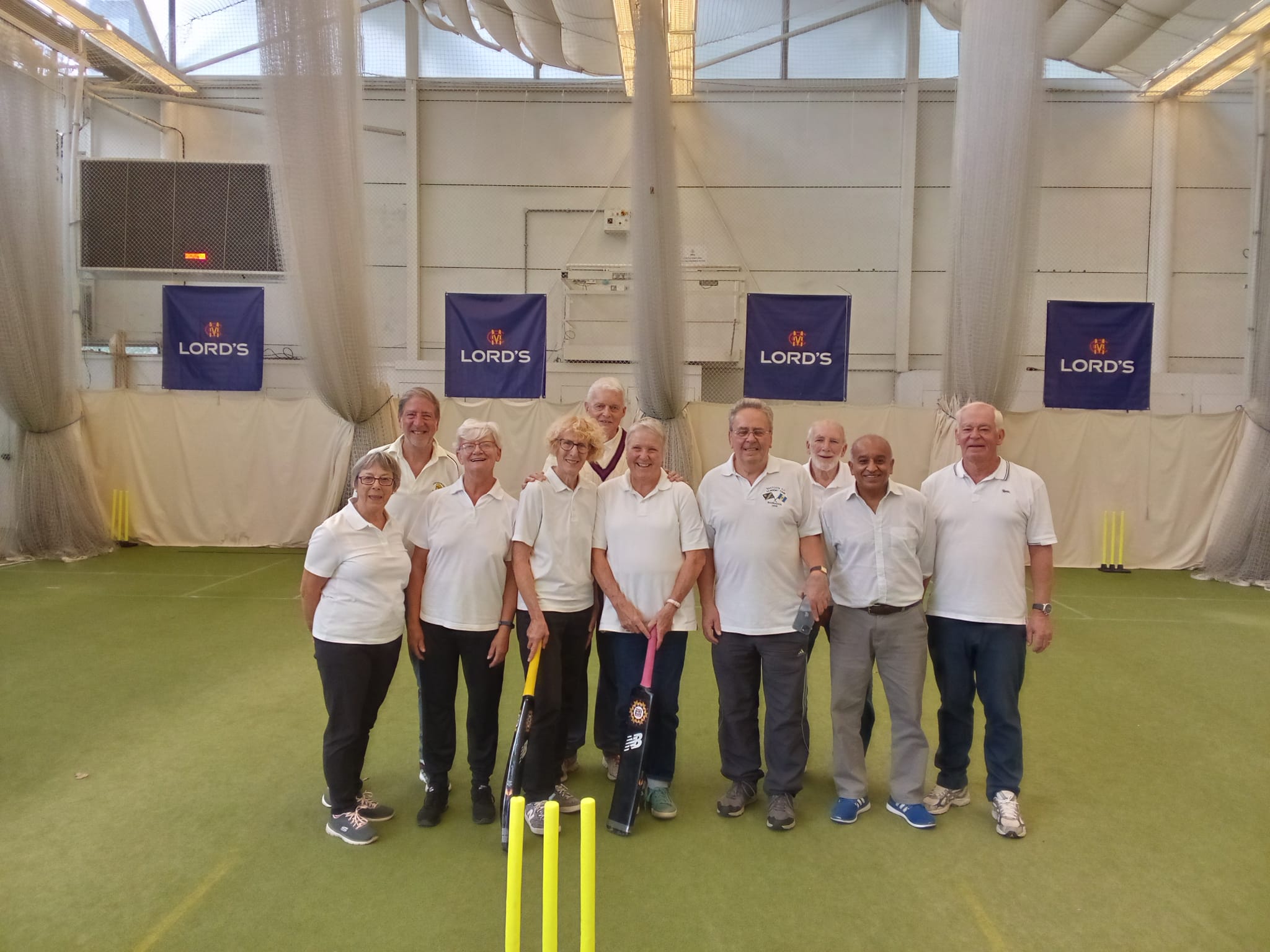 members in cricket whites pose in an indoor cricket centre