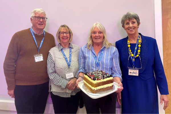 four u3a members smile for the camera with a large celebration cake
