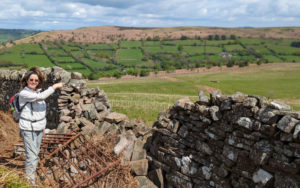 A woman points over a stone fence to a field where there are tiny sapling trees