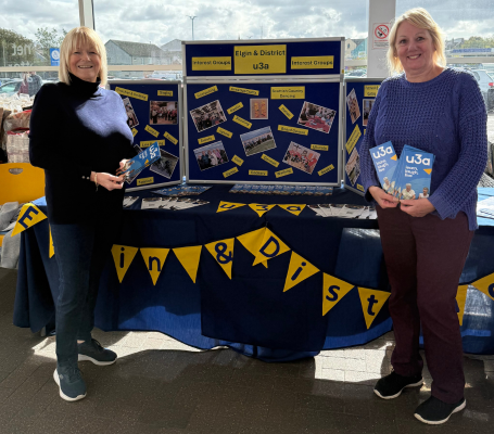 two women stand in front of a publicity stand holding leaflets